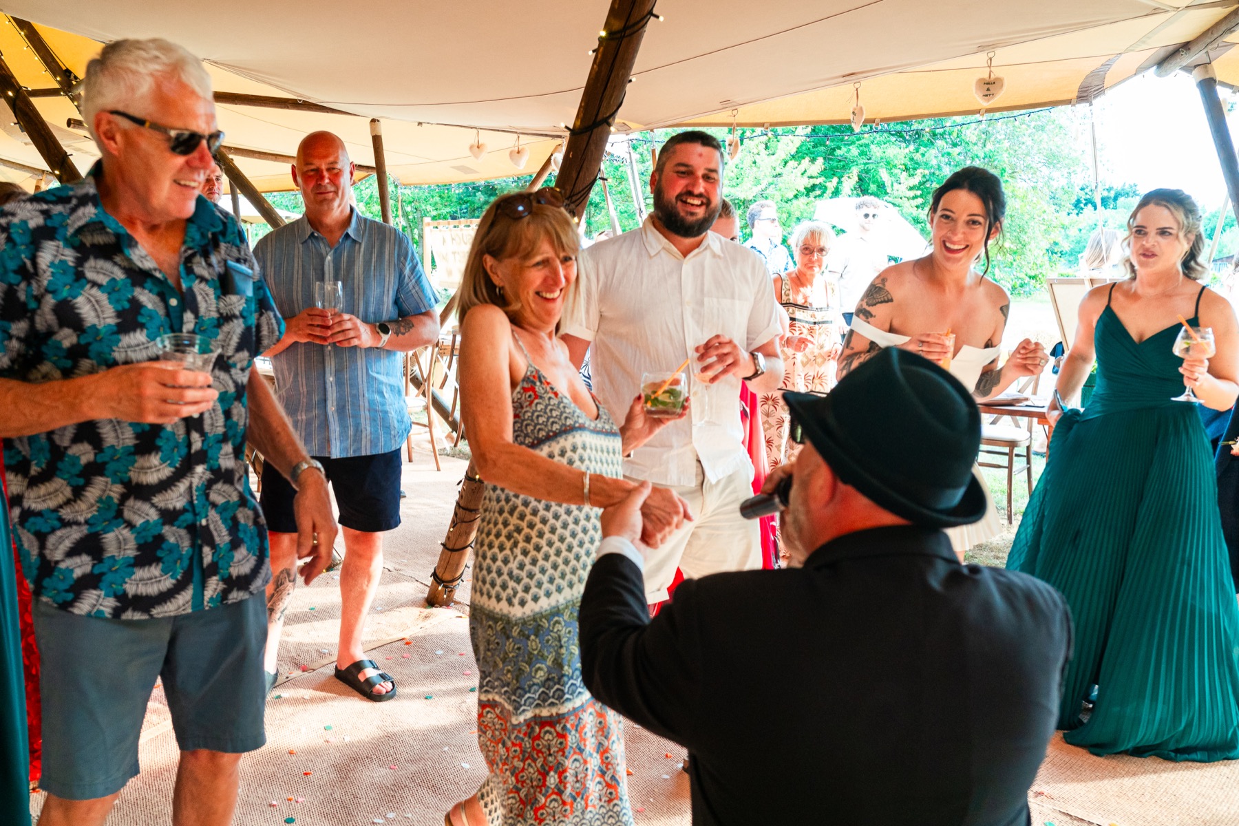 A performer in a Blues Brothers hat interacting with smiling wedding guests