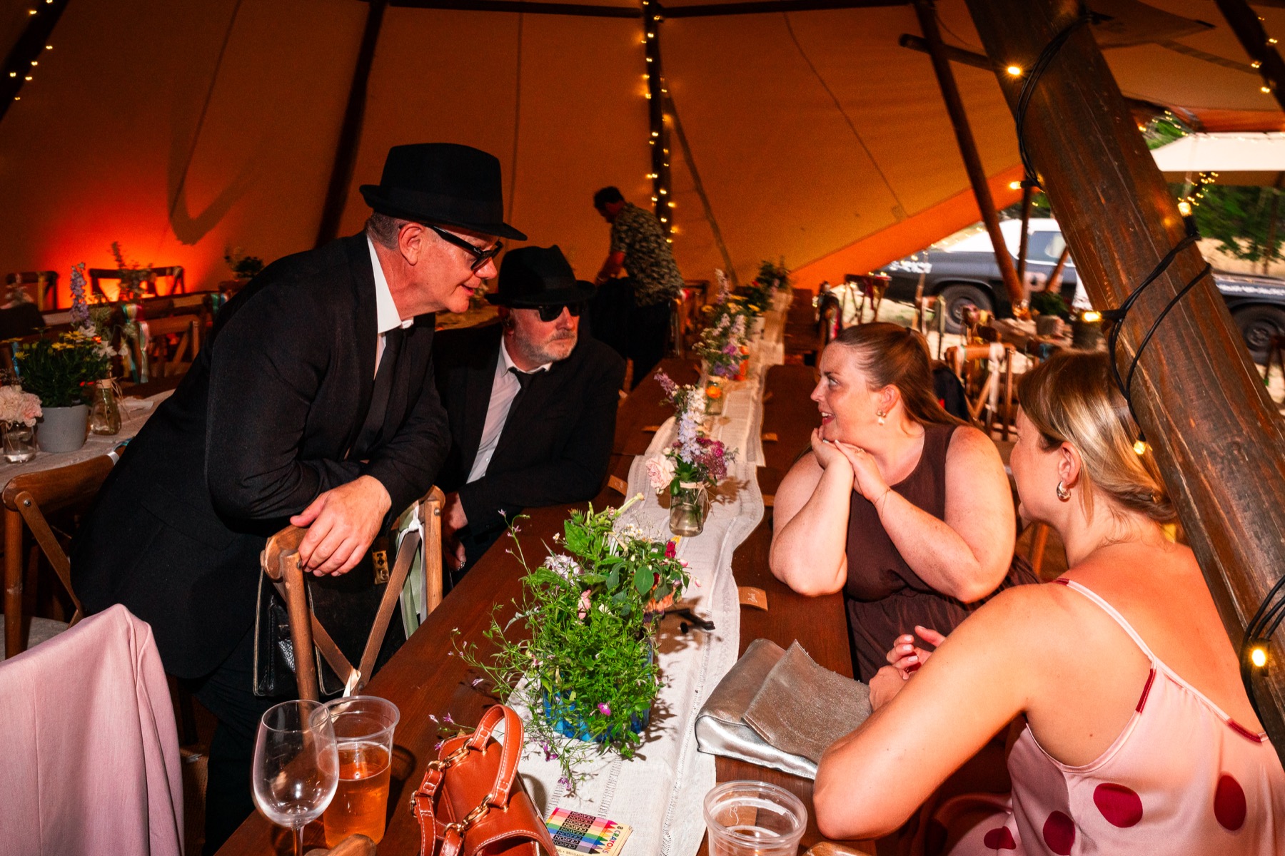 Jake and Elwood talking with a smiling wedding guest at her table